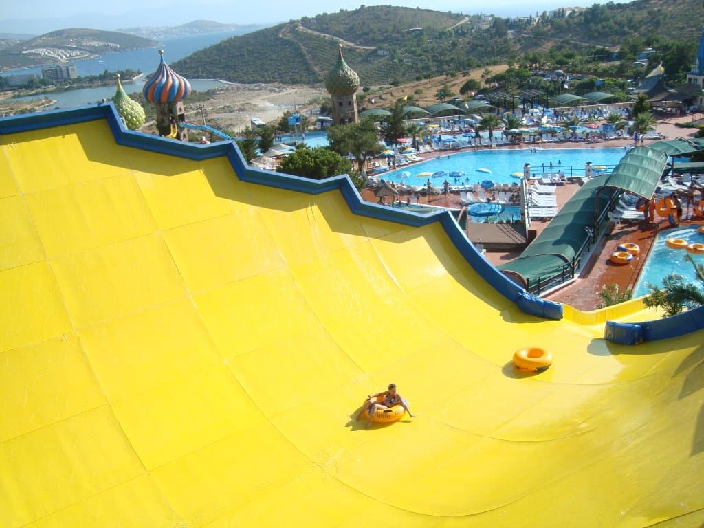 Bright twisting waterslides curving above a sunny aquapark pool.