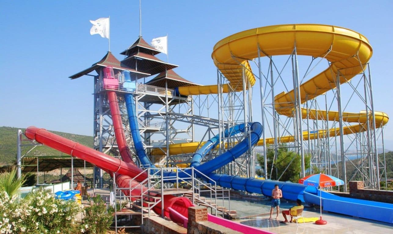 Bright twisting waterslides curving above a sunny aquapark pool.