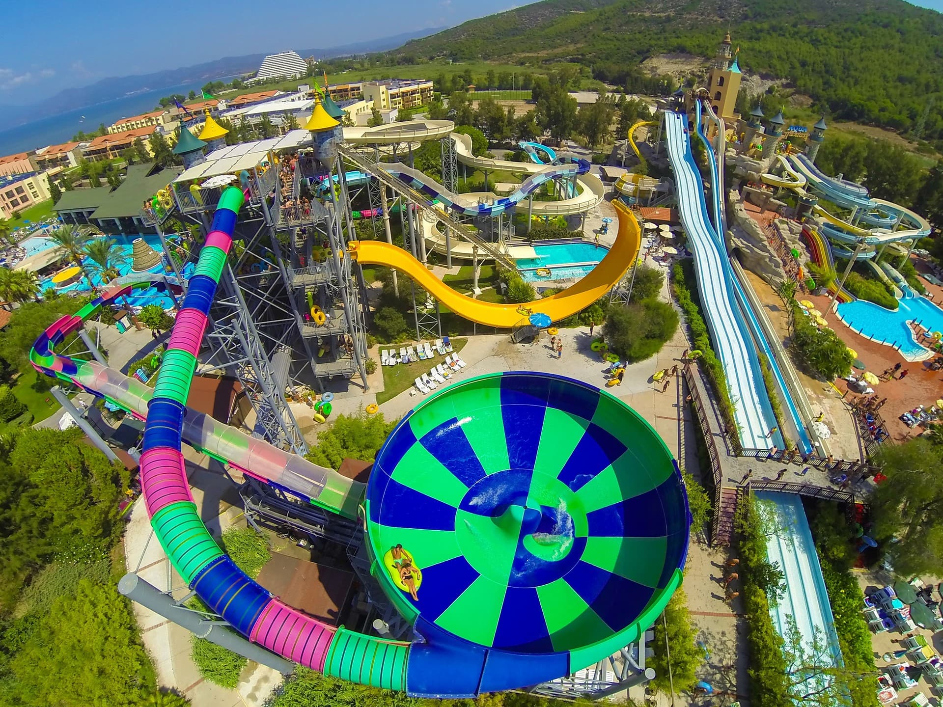 Bright twisting waterslides curving above a sunny aquapark pool.