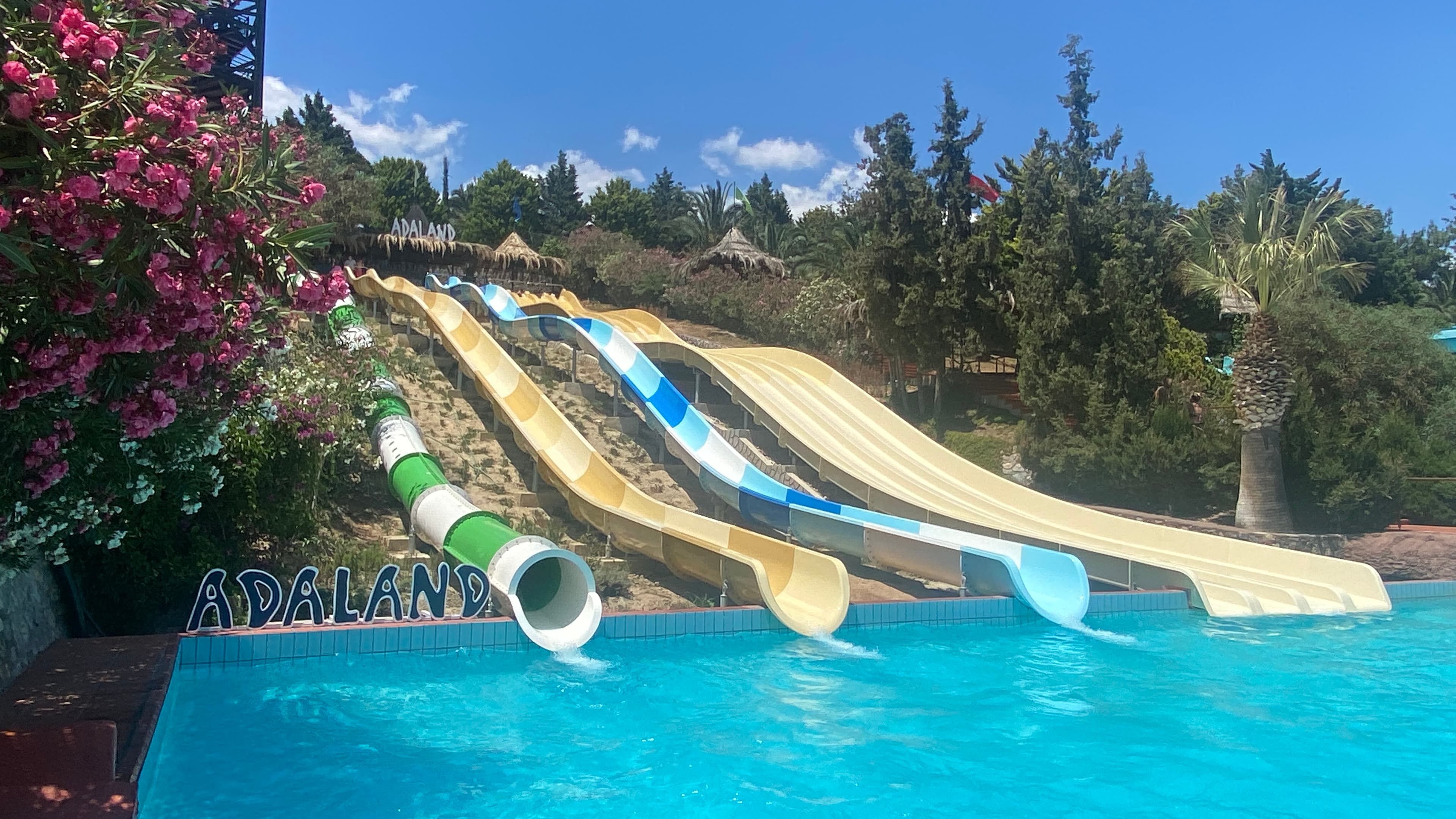 Bright twisting waterslides curving above a sunny aquapark pool.