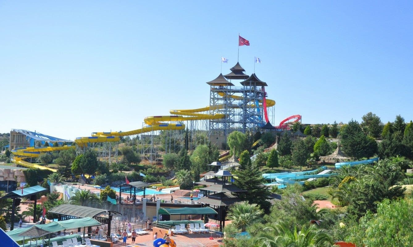 Bright twisting waterslides curving above a sunny aquapark pool.