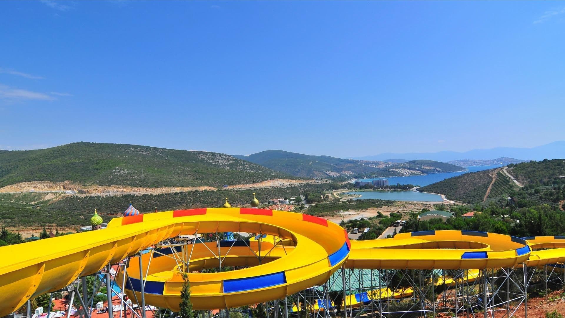 Bright twisting waterslides curving above a sunny aquapark pool.