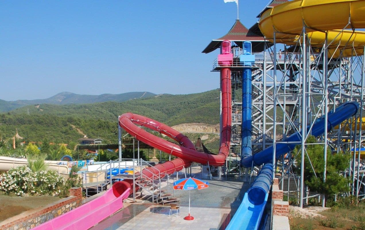 Bright twisting waterslides curving above a sunny aquapark pool.