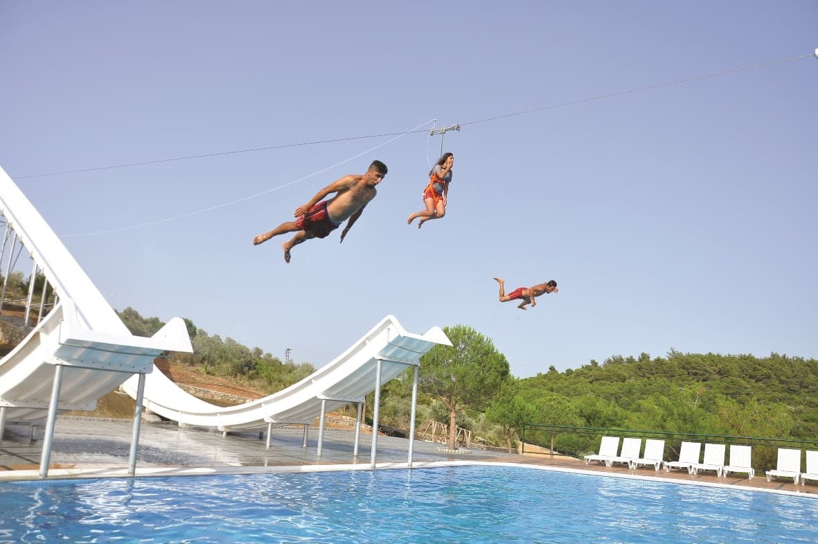 Bright twisting waterslides curving above a sunny aquapark pool.