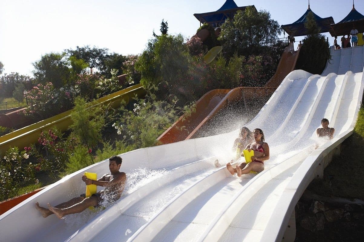 Bright twisting waterslides curving above a sunny aquapark pool.