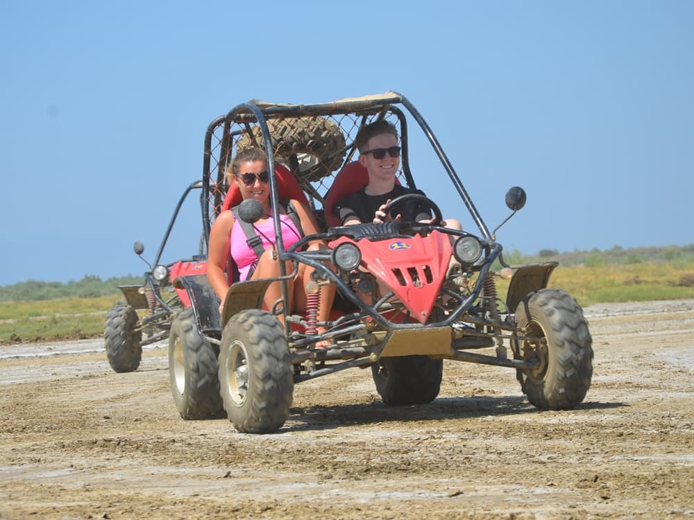 A two-seater UTV buggy splashing through mud on a rugged forest track.
