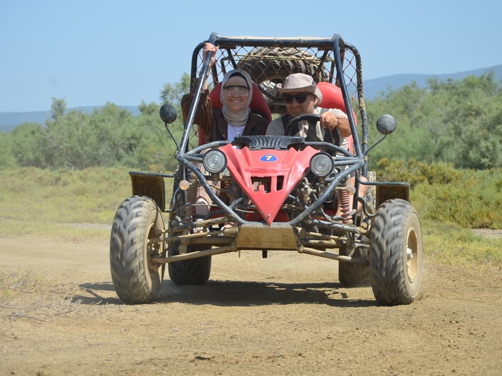 A two-seater UTV buggy splashing through mud on a rugged forest track.