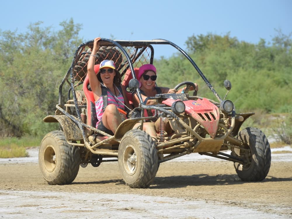 A two-seater UTV buggy splashing through mud on a rugged forest track.
