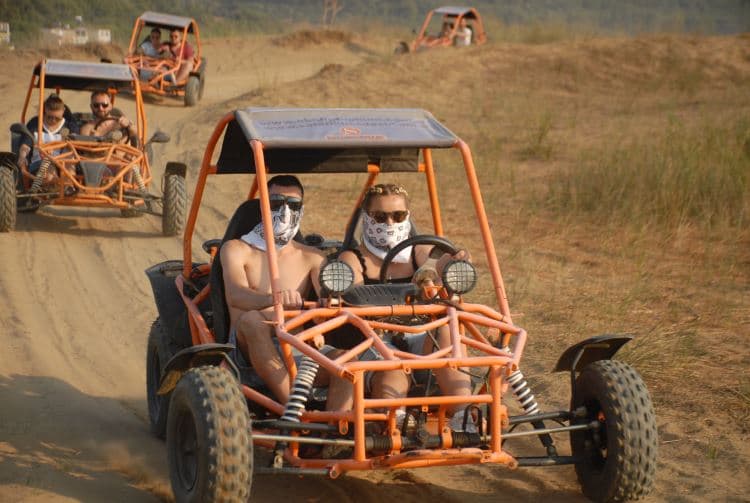 A two-seater UTV buggy splashing through mud on a rugged forest track.