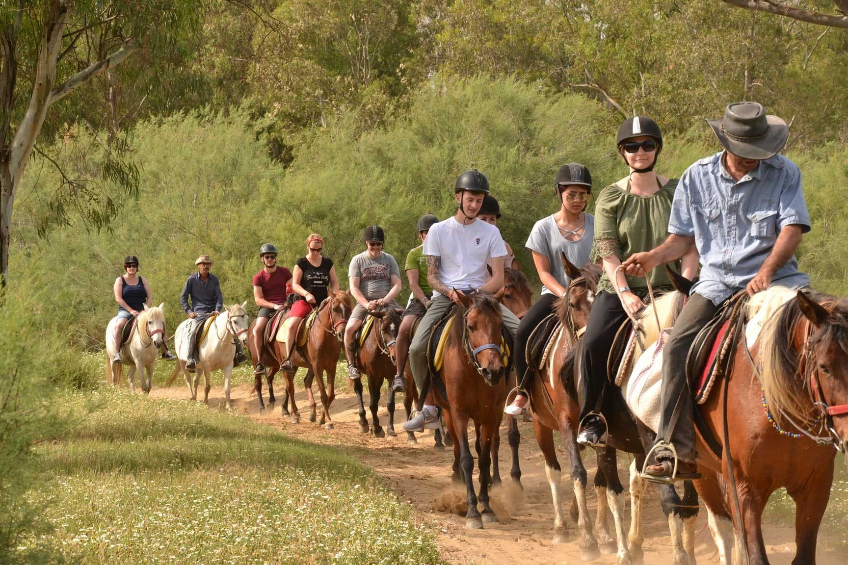 Riders on horseback following a coastal trail at sunset above the Aegean.