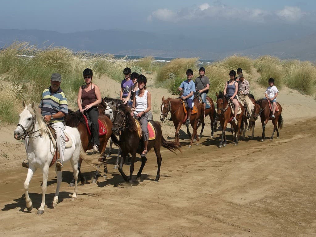 Riders on horseback following a coastal trail at sunset above the Aegean.
